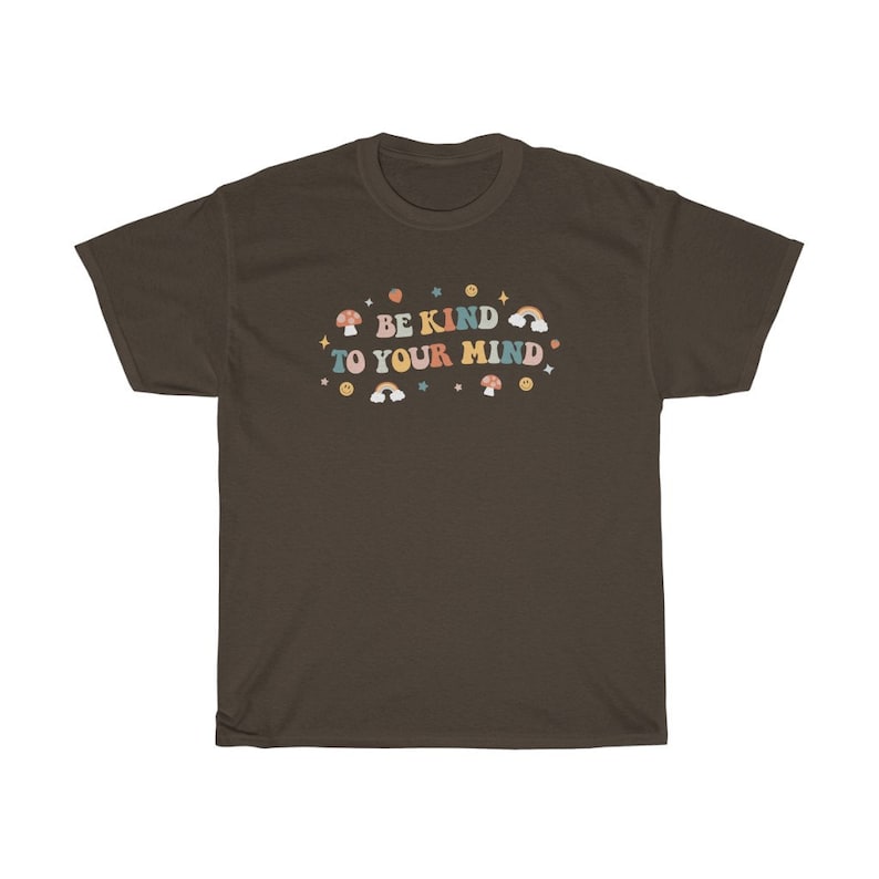 Puede incluir: Una camiseta marr&oacute;n con el texto "BE KIND TO YOUR MIND" en letras retro de colores. El texto est&aacute; rodeado de peque&ntilde;as ilustraciones de setas, arco&iacute;ris y estrellas.