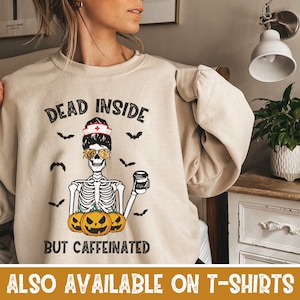 May include: A beige sweatshirt with a graphic of a skeleton wearing a nurse's hat and sunglasses, holding a cup of coffee. The text on the sweatshirt reads "Dead Inside But Caffeinated".
