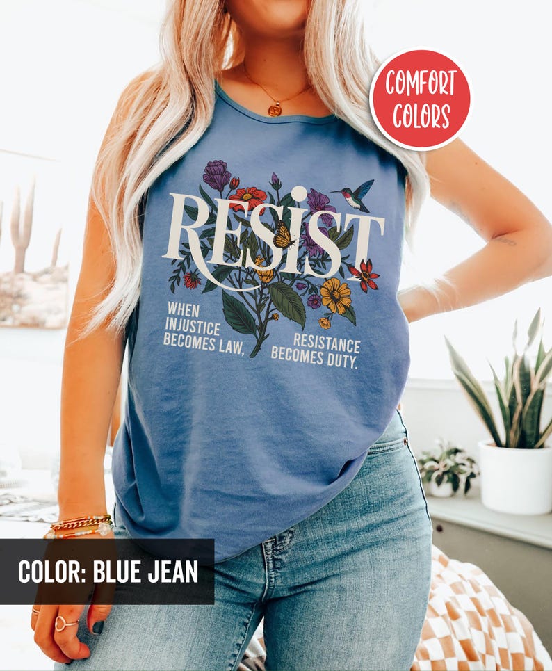 May include: A blue jean tank top with the word "RESIST" in white lettering surrounded by colorful flowers and a hummingbird. The text "WHEN INJUSTICE BECOMES LAW, RESISTANCE BECOMES DUTY." is printed below the word "RESIST".