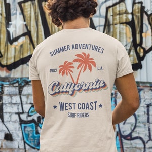May include: A beige t-shirt with a retro-style graphic design featuring palm trees, the text "Summer Adventures", "1982", "California", "L.A.", "West Coast", and "Surf Riders".