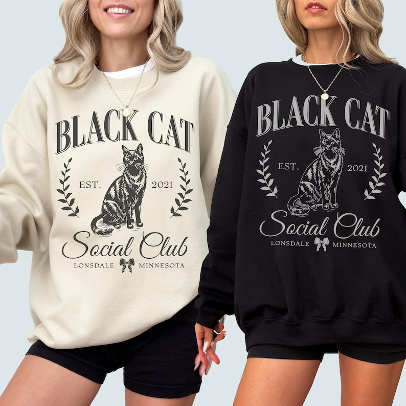 May include: Two black sweatshirts with a black cat graphic and the text "Black Cat Social Club Est. 2021 Lonsdale Minnesota". One sweatshirt is cream colored and the other is black.