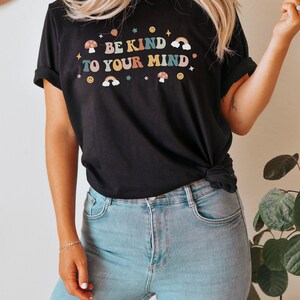 Puede incluir: Una camiseta negra con un gr&aacute;fico de arco&iacute;ris, hongo y estrella. El texto en la camiseta dice "Be Kind To Your Mind".