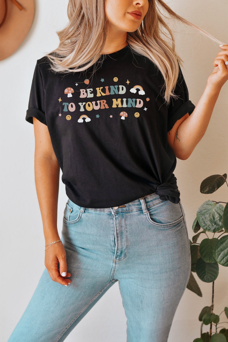 Puede incluir: Una camiseta negra con un gr&aacute;fico de arco&iacute;ris, hongo y estrella. El texto en la camiseta dice "Be Kind To Your Mind".
