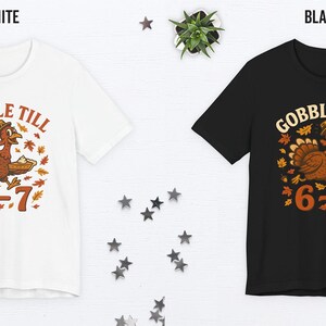 K&ouml;nnte beinhalten: Wei&szlig;e und schwarze T-Shirts mit einem Thanksgiving-Motiv. Das Design zeigt einen Cartoon-Truthahn mit dem Text "GOBBLE TILL" dar&uuml;ber und "6=7" darunter. Der Truthahn ist braun, mit orangefarbenen und gelben Akzenten.