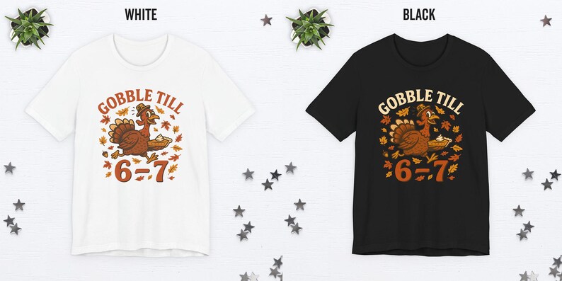 K&ouml;nnte beinhalten: Wei&szlig;e und schwarze T-Shirts mit einem Thanksgiving-Motiv. Das Design zeigt einen Cartoon-Truthahn mit dem Text "GOBBLE TILL" dar&uuml;ber und "6=7" darunter. Der Truthahn ist braun, mit orangefarbenen und gelben Akzenten.