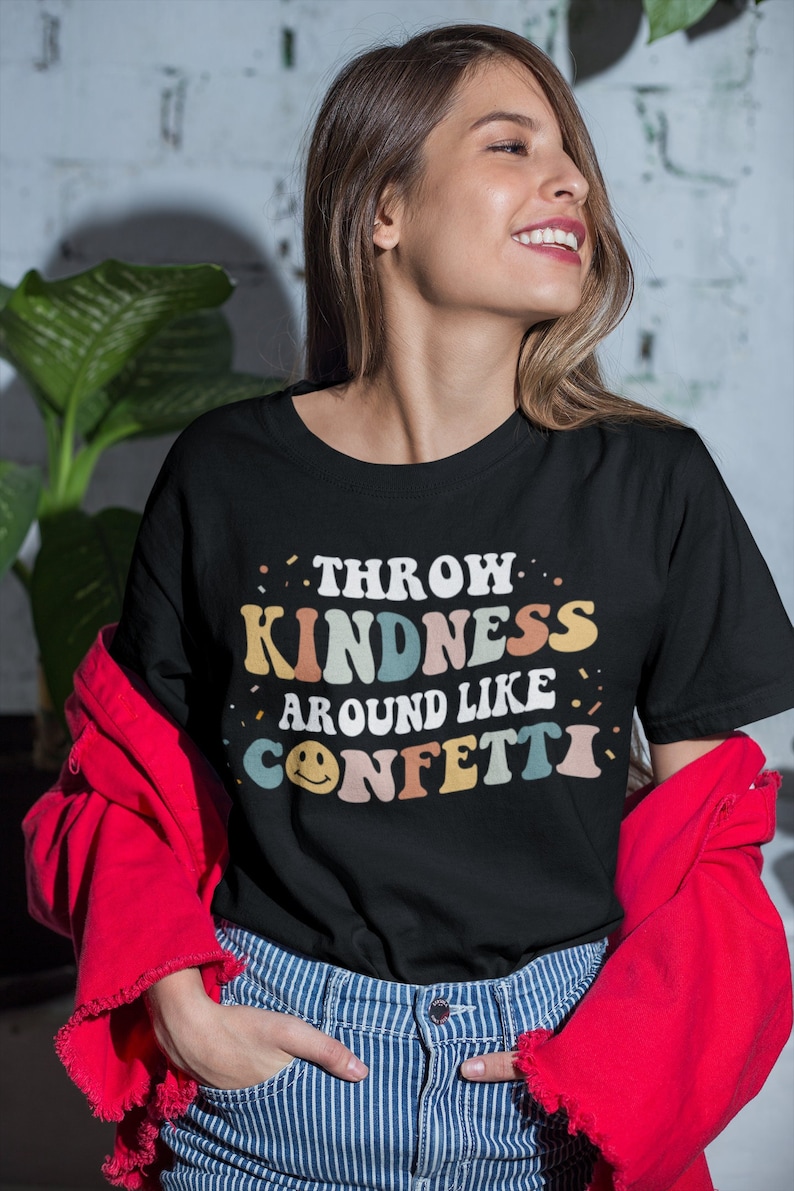 May include: A black t-shirt with a retro-style graphic that says "Throw Kindness Around Like Confetti". The graphic is in rainbow colours with a smiley face.