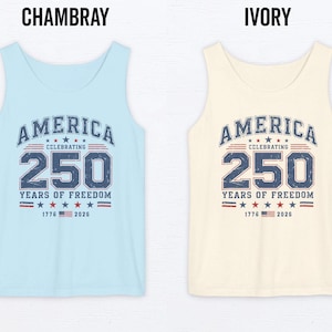 以下が含まれることがあります： 水色とアイボリーのタンクトップ2枚。紺色と赤色で「AMERICA CELEBRATING 250 YEARS OF FREEDOM」の文字。デザインには星と1776年と2026年の文字が含まれています。