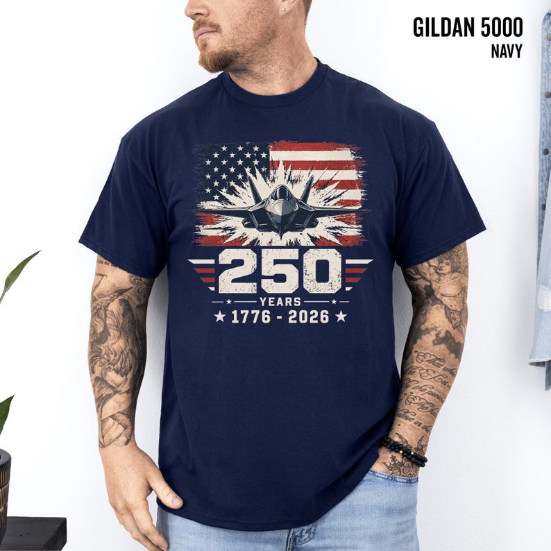 May include: Navy blue Gildan 5000 t-shirt featuring a graphic of a fighter jet in front of a distressed American flag. The design includes the text "250 YEARS 1776-2026".