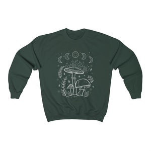 May include: A dark green sweatshirt featuring a white outline of mushrooms and a crescent moon design. The design includes a large mushroom with a smaller mushroom on either side. The design also includes a crescent moon with stars.