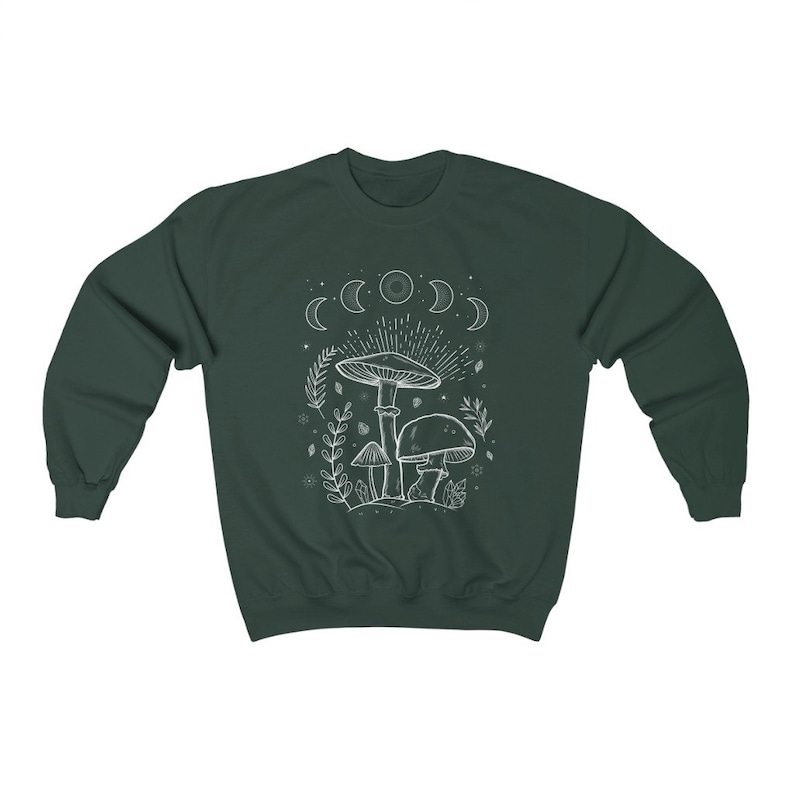 May include: A dark green sweatshirt featuring a white outline of mushrooms and a crescent moon design. The design includes a large mushroom with a smaller mushroom on either side. The design also includes a crescent moon with stars.