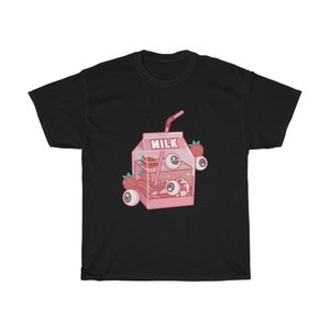 Puede incluir: Camiseta negra con una ilustraci&oacute;n de dibujos animados rosa de un cart&oacute;n de leche con fresas y ojos. El cart&oacute;n dice "MILK".