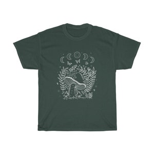 以下が含まれることがあります： 暗い緑色のTシャツに、白い森の風景の中にキノコが描かれたグラフィックがプリントされています。グラフィックには、月、蝶、葉っぱが含まれています。