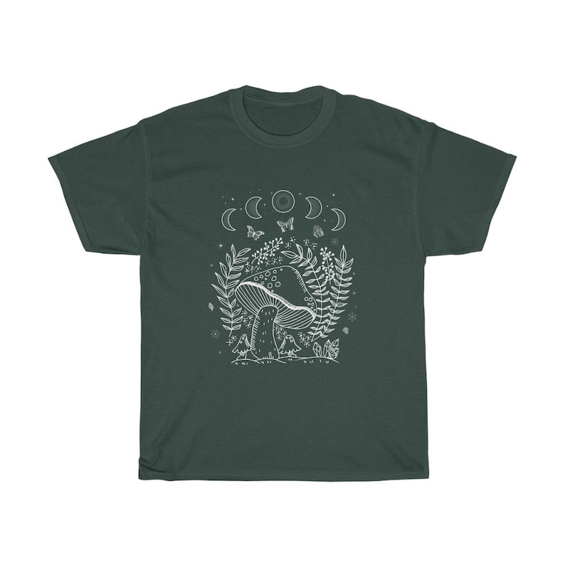 以下が含まれることがあります： 暗い緑色のTシャツに、白い森の風景の中にキノコが描かれたグラフィックがプリントされています。グラフィックには、月、蝶、葉っぱが含まれています。