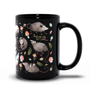 May include: Black ceramic mug with a white and gray opossum pattern. The opossums are surrounded by flowers, leaves, and mushrooms.