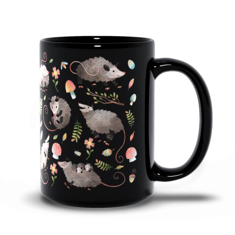 May include: Black ceramic mug with a white and gray opossum pattern. The opossums are surrounded by flowers, leaves, and mushrooms.