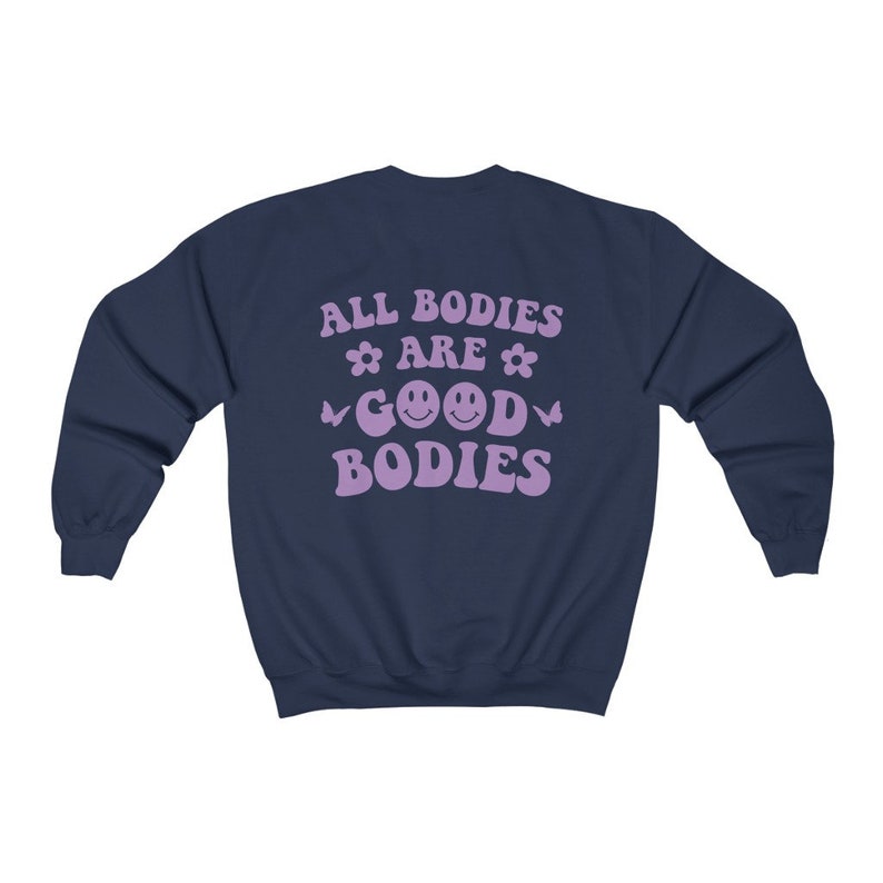 May include: Navy blue sweatshirt with lavender text reading "ALL BODIES ARE GOOD BODIES". The design includes flowers, butterflies, and smiley faces. A casual, comfortable style of clothing.
