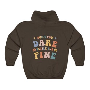 Puede incluir: Sudadera con capucha marr&oacute;n con el texto "Don't you dare settle for fine" en letras de colores.
