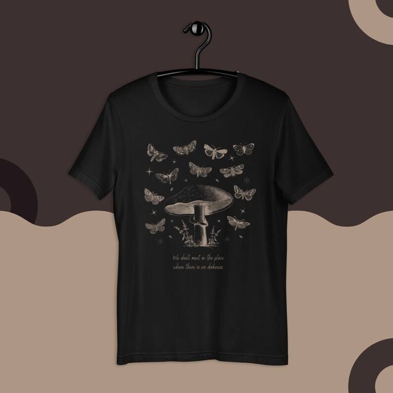 May include: Black t-shirt with a graphic print of a mushroom with butterflies and the text "We shall meet in the place where there is no darkness".