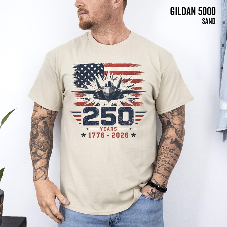 May include: Sand-colored Gildan 5000 t-shirt featuring a graphic of an American flag, a jet, and the text "250 YEARS 1776-2026". The design is in red, white, and blue.