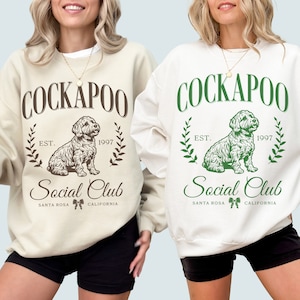 May include: Two white sweatshirts with a brown and green graphic design. The design features a dog, the text "Cockapoo", "Est. 1997", and "Social Club". The text "Santa Rosa, California" is also included in the design.
