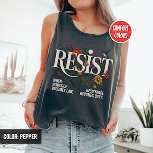 May include: A dark gray tank top with the word "RESIST" in white lettering and a floral design. The text below the word "RESIST" reads "When injustice becomes law, resistance becomes duty."