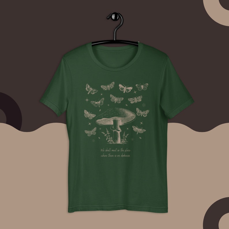 May include: A dark green t-shirt with a white graphic print of a mushroom with butterflies flying around it. The text "We shall meet in the place where there is no darkness" is printed below the mushroom.