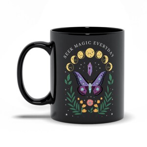 May include: Black ceramic mug with a white design featuring a purple butterfly, a crystal, and a crescent moon phase cycle. The text "Seek Magic Everyday" is written in a white circular font around the moon phases.