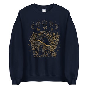 Op de afbeelding: Navyblauwe trui met een gouden omtrekillustratie van een paddenstoel, bladeren en halve manen. De tekst "Shroom Queens" is op de trui gedrukt.