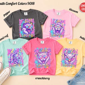 May include: Five short-sleeve t-shirts in pepper, blossom, island reef, crunchberry, and butter colors. Each shirt features a graphic of an animal or knight wearing star or heart-shaped sunglasses, with text reading Falcons, Lions, Knights, Wildcats, or Owls.