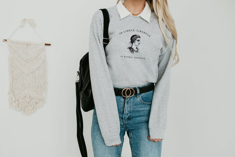 May include: Grey sweatshirt with a black and white illustration of a woman's face and the text "In Libras, Libertas. In Books, Freedom."