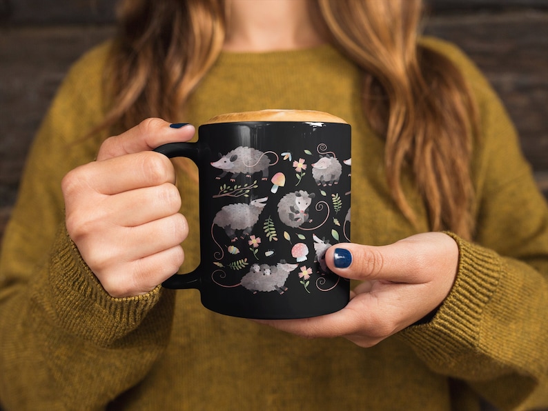 May include: Black ceramic coffee mug with a white design of opossums, mushrooms, and flowers.