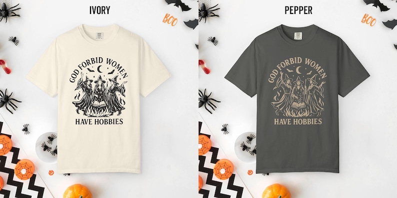 May include: Two short-sleeve crew neck t-shirts, one in ivory and one in pepper gray. Both feature a black graphic print of three witches around a cauldron with the text "GOD FORBID WOMEN HAVE HOBBIES" arched above and printed below the illustration.