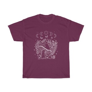 以下が含まれることがあります： 森の風景の中にキノコが描かれた、マルーンのTシャツ。白いグラフィックで、三日月、蝶、その他の葉っぱが描かれています。