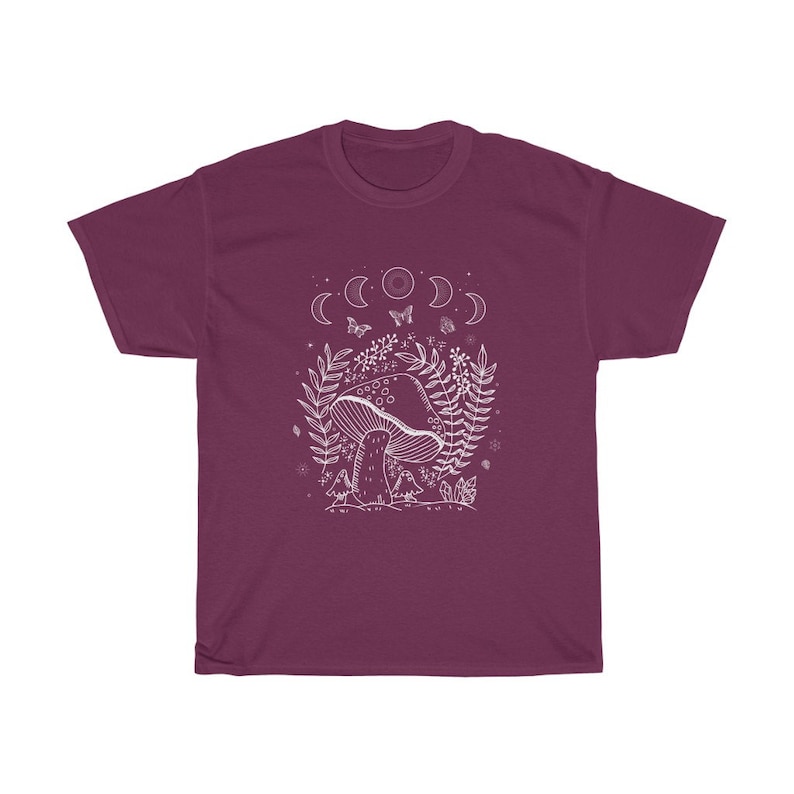 以下が含まれることがあります： 森の風景の中にキノコが描かれた、マルーンのTシャツ。白いグラフィックで、三日月、蝶、その他の葉っぱが描かれています。