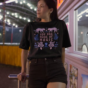 May include: A black t-shirt with a pink and blue graphic design featuring snakes, stars, and the text "You are made of magic".