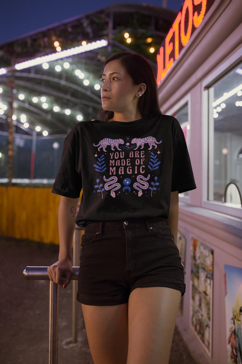 May include: A black t-shirt with a pink and blue graphic design featuring snakes, stars, and the text "You are made of magic".