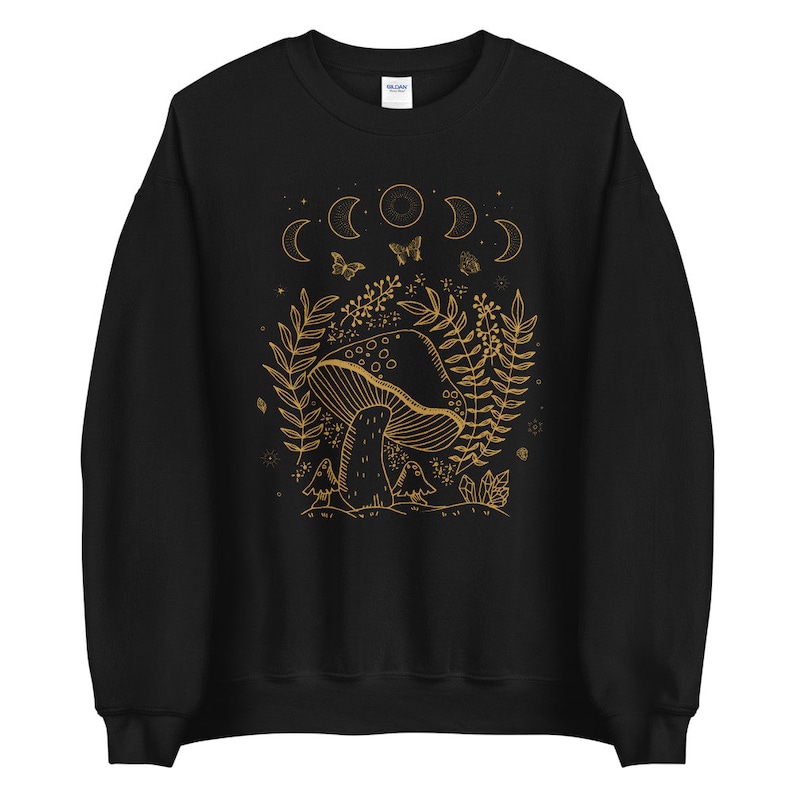 Op de afbeelding: Zwart sweatshirt met een gouden omtrek van een paddenstoel, maanfasen en vlinders. Het ontwerp is gecentreerd op de voorkant van het sweatshirt.