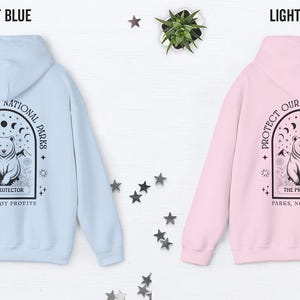 May include: Light blue and light pink hoodies with a graphic on the back. The graphic features a bear inside an arch with the text "PROTECT OUR NATIONAL PARKS" and "THE PROTECTOR PARKS, NOT PROFITS".