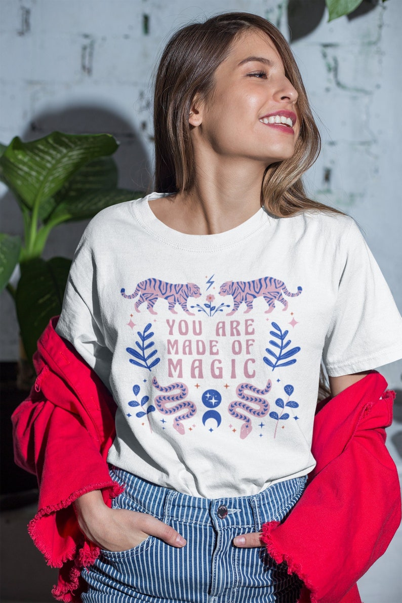 May include: White t-shirt with a pink and blue graphic design featuring tigers, snakes, and the text "You are made of magic".