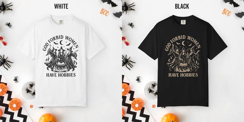 May include: A white t-shirt and a black t-shirt, each featuring a graphic print of three witches around a campfire with the text 'GOD FORBID WOMEN HAVE HOBBIES' arched above and below the illustration, surrounded by stars, bats, and a crescent moon.