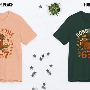 K&ouml;nnte beinhalten: Zwei kurz&auml;rmelige T-Shirts, eines in Heather Peach und eines in Forest Green, jeweils mit einem Thanksgiving-Motiv. Die Grafik zeigt einen Cartoon-Truthahn mit einem Kuchen, umgeben von Bl&auml;ttern, und den Text "GOBBLE TILL 6=7".