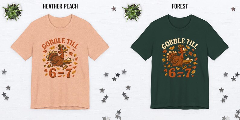 K&ouml;nnte beinhalten: Zwei kurz&auml;rmelige T-Shirts, eines in Heather Peach und eines in Forest Green, jeweils mit einem Thanksgiving-Motiv. Die Grafik zeigt einen Cartoon-Truthahn mit einem Kuchen, umgeben von Bl&auml;ttern, und den Text "GOBBLE TILL 6=7".