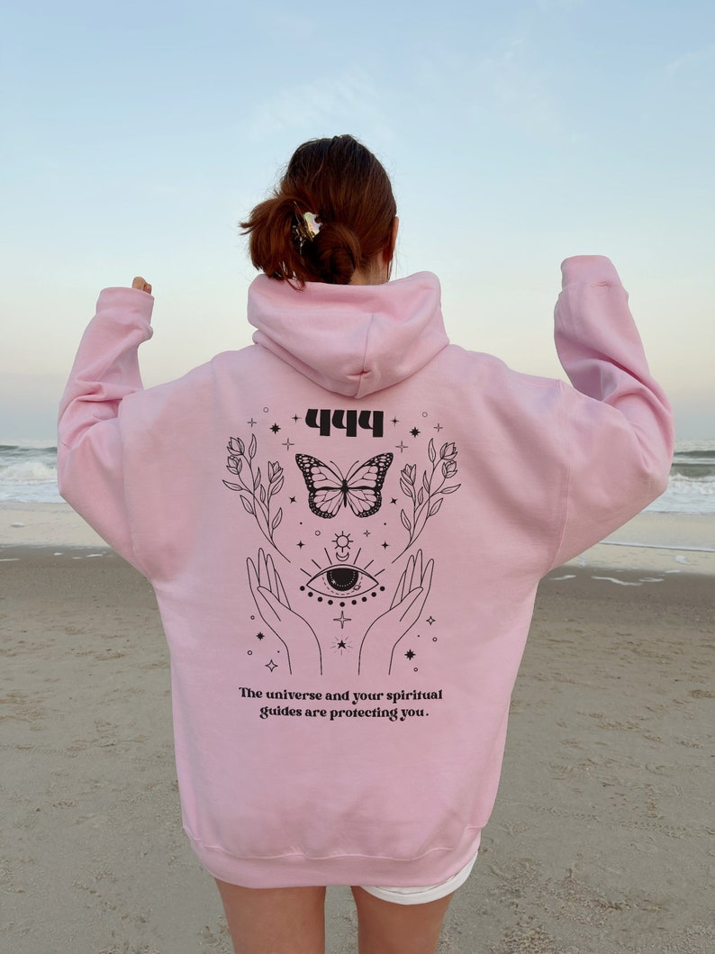 May include: Pink hoodie with a black graphic design featuring a butterfly, an eye, and the text "444 The universe and your spiritual guides are protecting you."