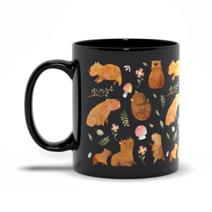 May include: Black ceramic mug with a white design of capybaras, mushrooms, and flowers. The capybaras are brown and white and are in various poses.
