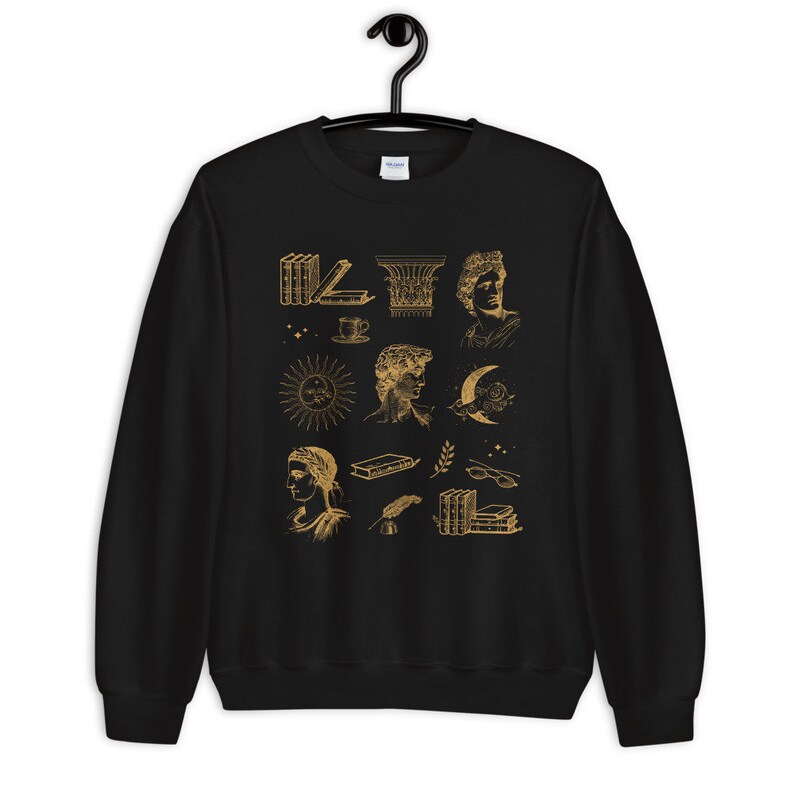 Puede incluir: Sudadera negra con un estampado dorado de varias ilustraciones que incluyen libros, un sol, una luna, una taza, una columna y algunas caras.