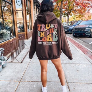 May include: Brown hooded sweatshirt with the text "TRUST IN THE LORD WITH ALL YOUR HEART PROVERBS 3:5" in colorful retro lettering.