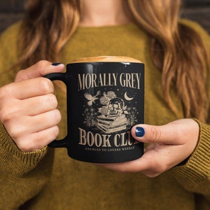 May include: Black coffee mug with a white design that says "Morally Grey Book Club" with a skull and flowers. The text below the design says "Enemies to Lovers Weekly."