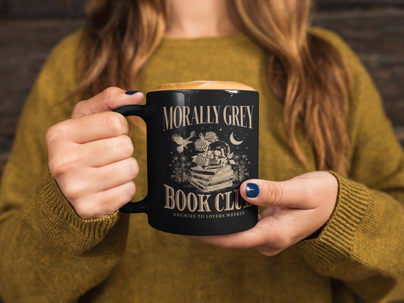 May include: Black coffee mug with a white design that says "Morally Grey Book Club" with a skull and flowers. The text below the design says "Enemies to Lovers Weekly."