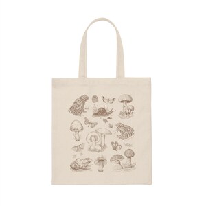 May include: A beige tote bag with a brown illustration of mushrooms, frogs, butterflies, and snails. The design is centered on the bag.