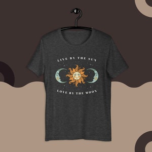 May include: A dark heather grey t-shirt with a sun and moon graphic and the text "Live by the sun, love by the moon".